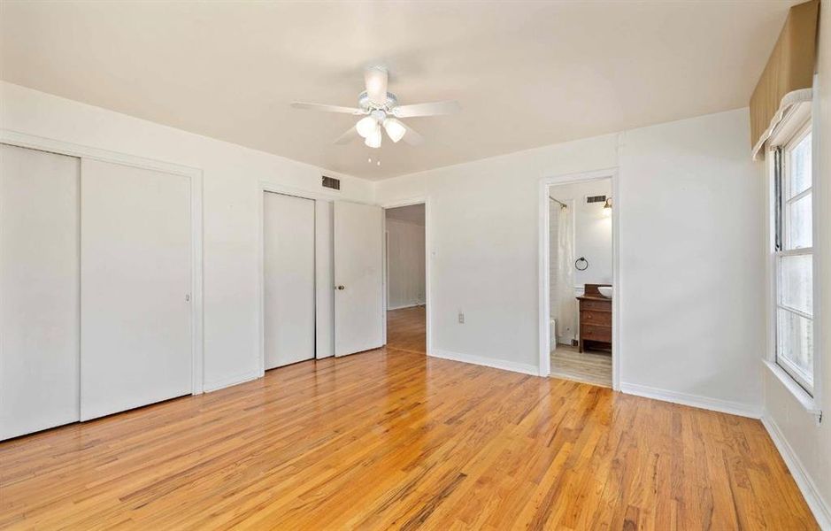 Unfurnished bedroom featuring multiple closets, light wood finished floors, ceiling fan, and ensuite bathroom