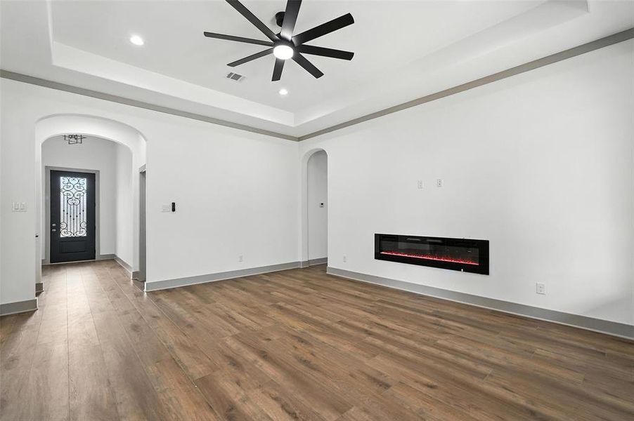 Unfurnished living room featuring a raised ceiling, dark wood-style flooring, arched walkways, a glass covered fireplace, and recessed lighting Unfurnished living room featuring a raised ceiling, dark wood-style flooring, arched walkways, a glass covered fireplace, and recessed lighting