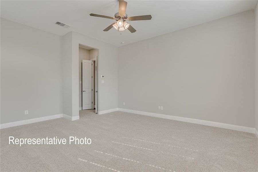 Spacious room featuring neutral carpeting, light gray walls, a ceiling fan with integrated lighting, white baseboards, and a doorway with a white paneled door