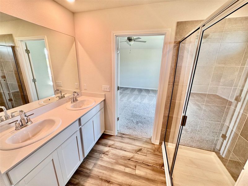 Bathroom featuring a stall shower, double vanity, light wood-style floors, and ceiling fan