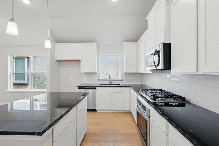 Kitchen with dark stone counters, light wood-style floors, hanging light fixtures, white cabinetry, and recessed lighting Kitchen with dark stone counters, light wood-style floors, hanging light fixtures, white cabinetry, and recessed lighting