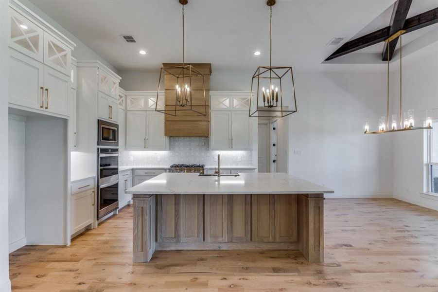 Kitchen featuring tasteful backsplash, white cabinets, light hardwood / wood-style flooring, decorative light fixtures, and a center island with sink