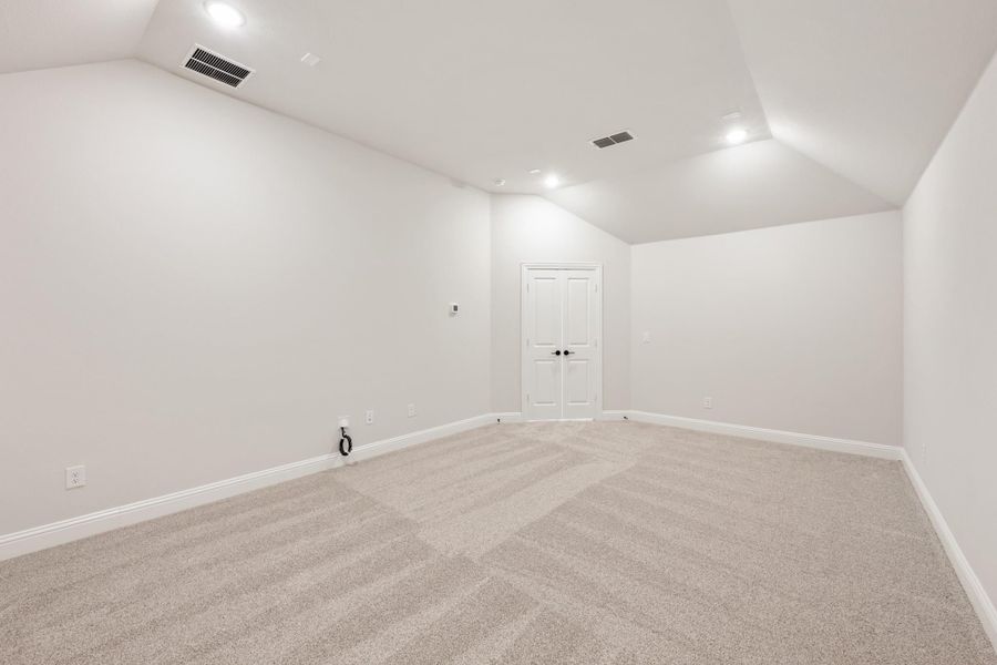 Empty room with vaulted ceiling, gray carpet, white walls, and double doors Empty room with vaulted ceiling, gray carpet, white walls, and double doors