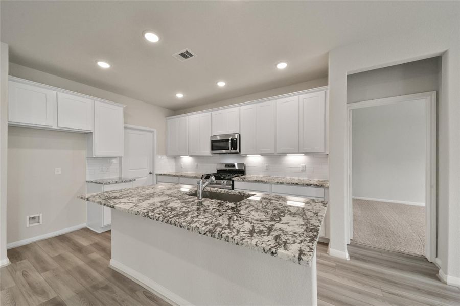 This photo shows a modern kitchen with white cabinetry, granite countertops, and stainless steel appliances. It features ample lighting and wood-look flooring, creating a bright and inviting space.