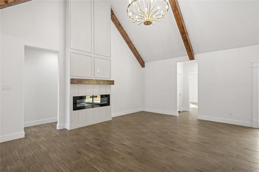 Unfurnished living room featuring lofted ceiling, a chandelier, a large fireplace, and dark wood-type flooring