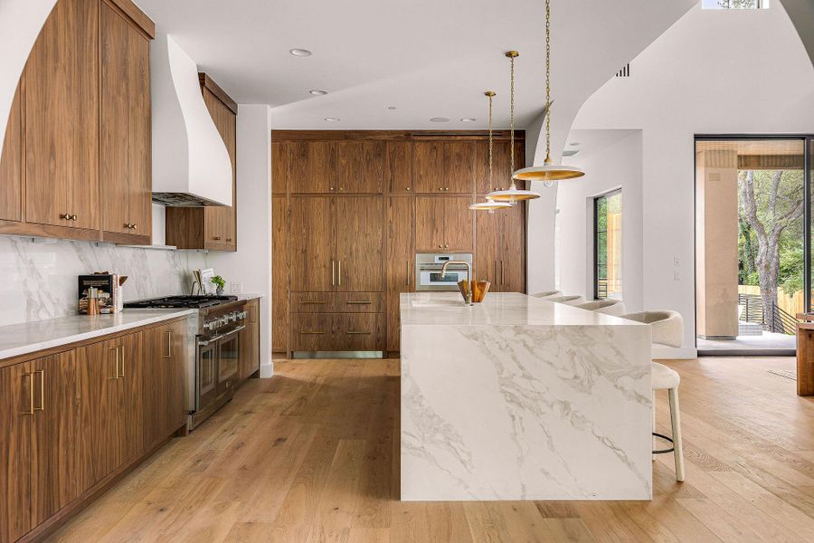 An inviting kitchen features warm wooden cabinetry, a grand marble island, and contemporary pendant lighting.