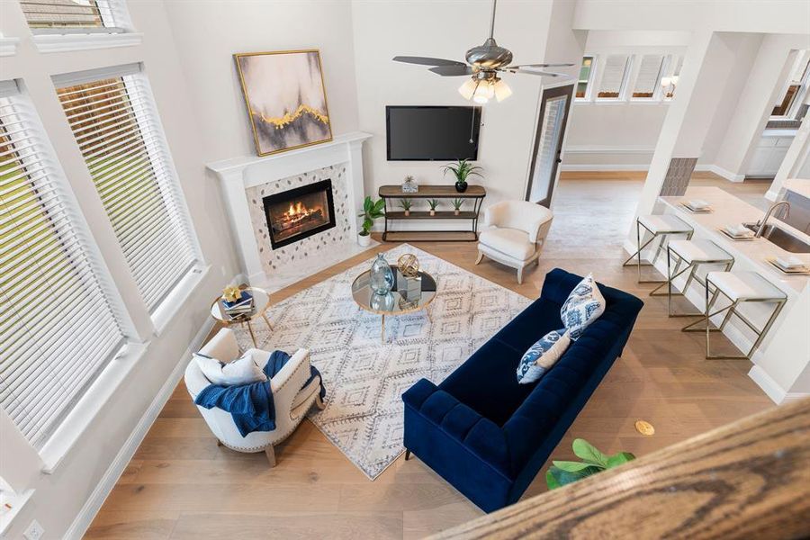 Living room featuring a fireplace, ceiling fan, light wood-type flooring, and a towering ceiling