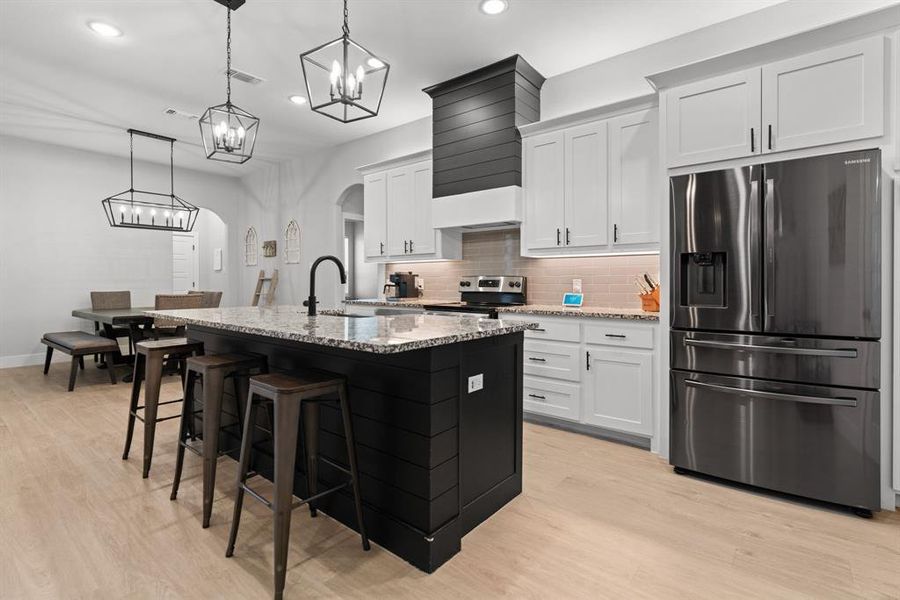 Kitchen with appliances with stainless steel finishes, light hardwood / wood-style flooring, pendant lighting, and white cabinetry