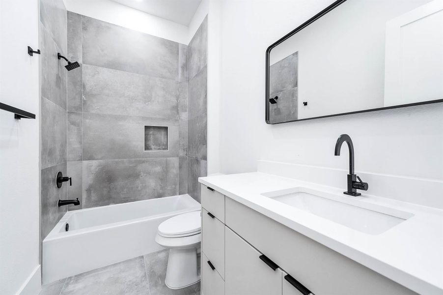 This modern bathroom features a sleek design with a gray-tiled shower and bathtub combo, a large mirror, and a stylish vanity with a black faucet. The space is bright and contemporary, offering a clean and fresh look.