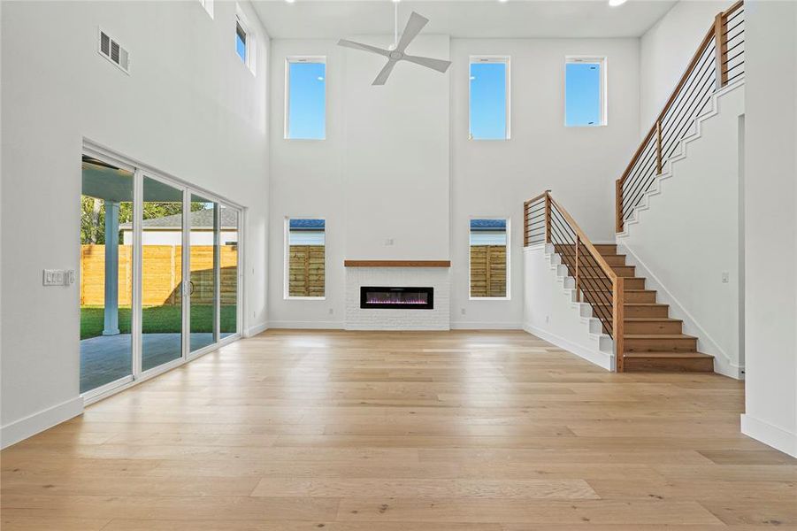Unfurnished living room featuring a glass covered fireplace, light wood-style floors, a ceiling fan, a towering ceiling, and stairway