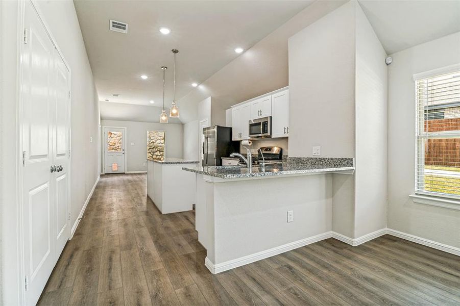 Open-concept kitchen and living area featuring wood-finish flooring, recessed lighting, and a kitchen island with pendant lights Open-concept kitchen and living area featuring wood-finish flooring, recessed lighting, and a kitchen island with pendant lights