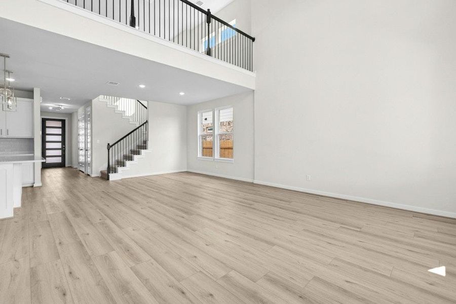 Unfurnished living room with a towering ceiling, light wood-type flooring, stairway, and recessed lighting