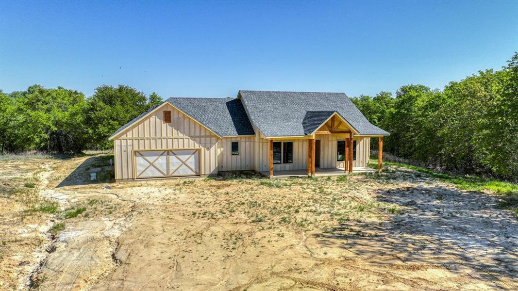 View of front of home with board and batten siding, dirt driveway, roof with shingles, an attached garage, and a porch View of front of home with board and batten siding, dirt driveway, roof with shingles, an attached garage, and a porch