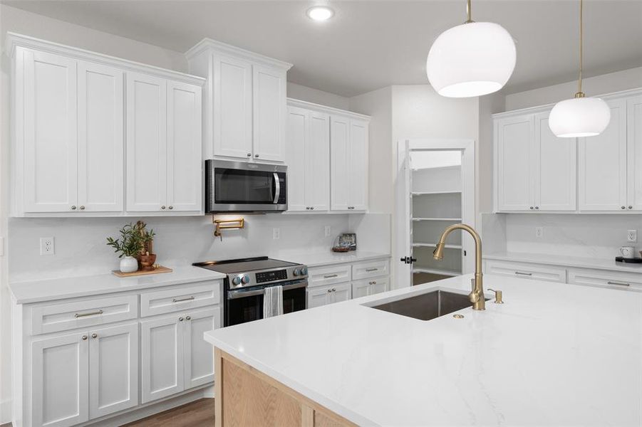 Kitchen with appliances with stainless steel finishes, a sink, white cabinetry, light countertops, and decorative light fixtures Kitchen with appliances with stainless steel finishes, a sink, white cabinetry, light countertops, and decorative light fixtures