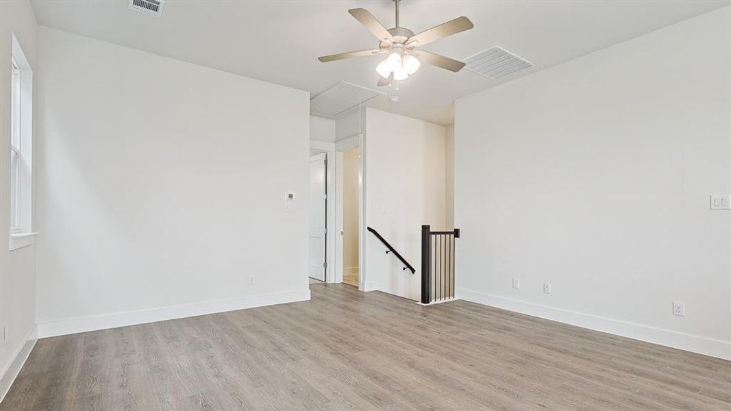 Spacious room featuring wood-finish flooring, a ceiling fan, and white baseboards