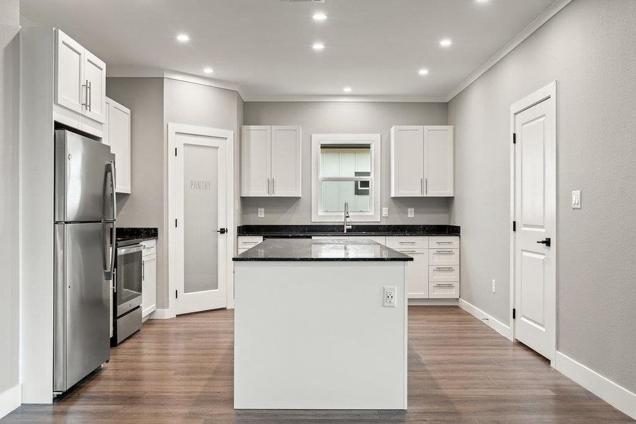 Kitchen featuring stainless steel appliances, white cabinetry, dark stone countertops, dark wood finished floors, and a center island