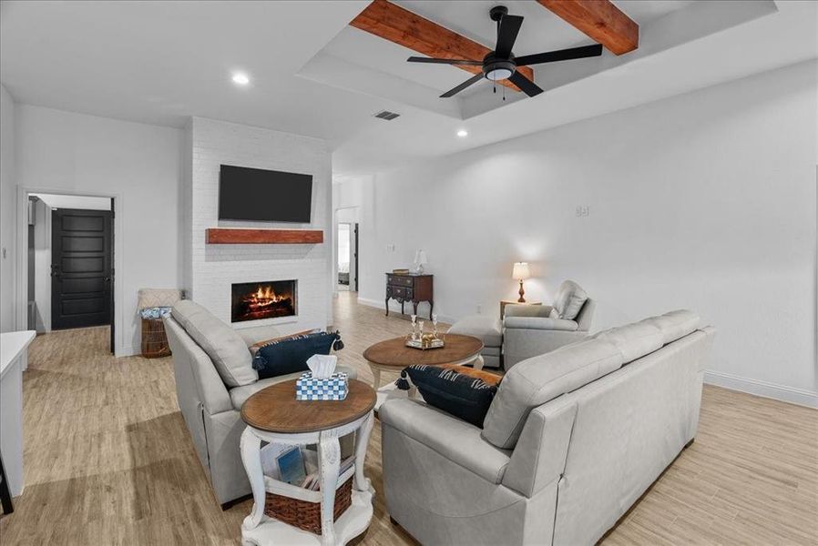 Living room featuring light wood-type flooring, a large fireplace, baseboards, and a ceiling fan