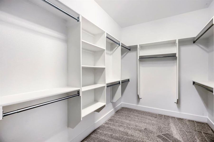 Walk-in closet featuring built-in shelving, multiple hanging rods, white trim, and patterned carpeting Walk-in closet featuring built-in shelving, multiple hanging rods, white trim, and patterned carpeting