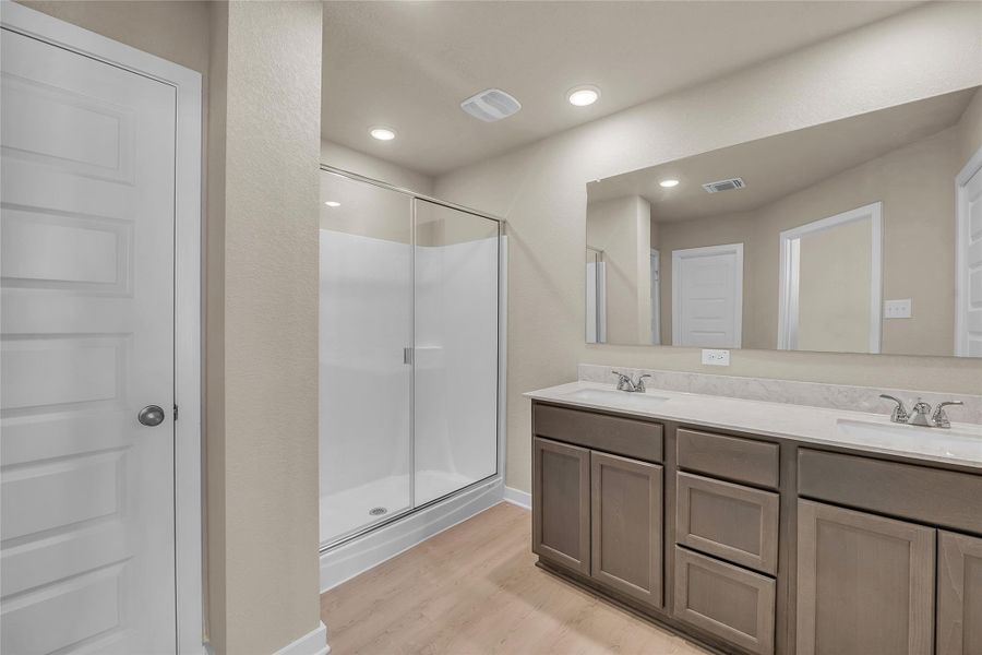 Full bath with double vanity, a stall shower, light wood-style floors, and recessed lighting