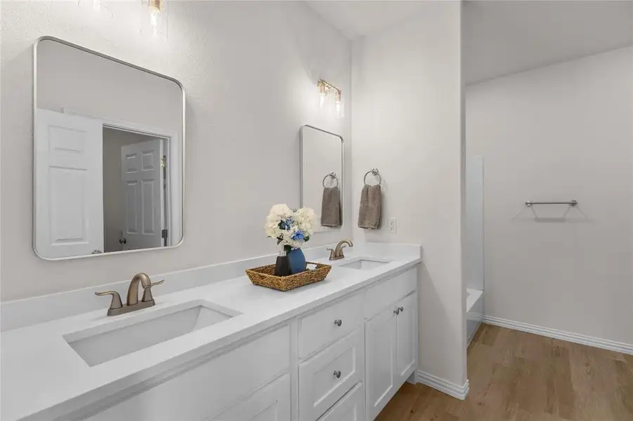 Bathroom featuring light wood finished floors, double vanity, and shower / tub combination