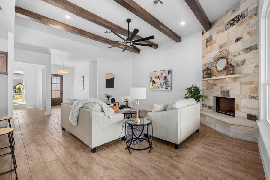 Living room with ceiling fan, a stone fireplace, light wood finished floors, beamed ceiling, and hanging lights