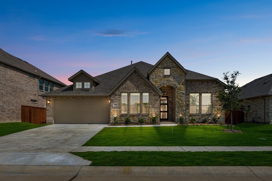 Single-story home with brick and stone exterior, two-car garage, arched entry, and green front lawn at dusk