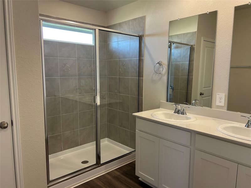 Full bathroom with a textured wall, a shower stall, double vanity, and dark wood-style flooring Full bathroom with a textured wall, a shower stall, double vanity, and dark wood-style flooring