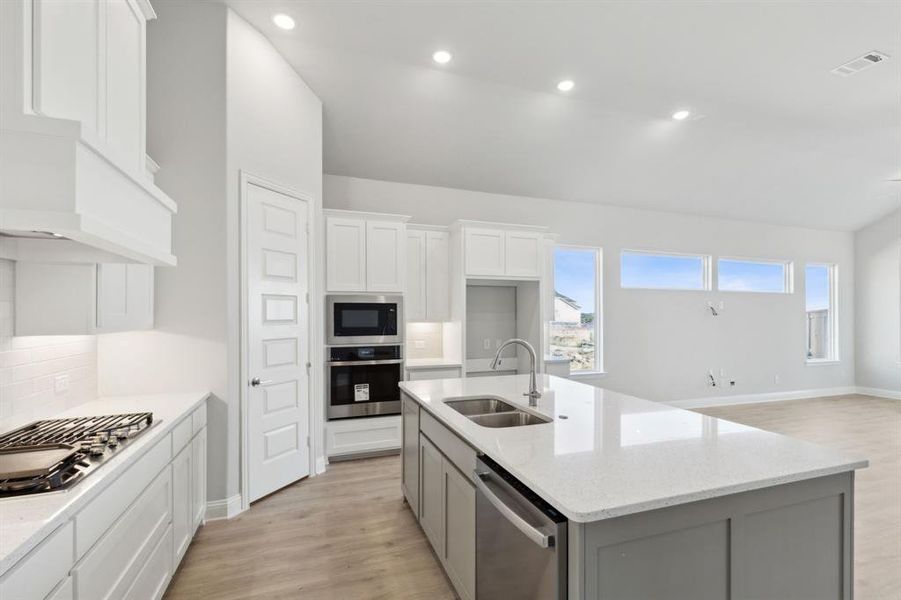 Kitchen with stainless steel appliances, a kitchen island with sink, sink, light hardwood / wood-style flooring, and white cabinets