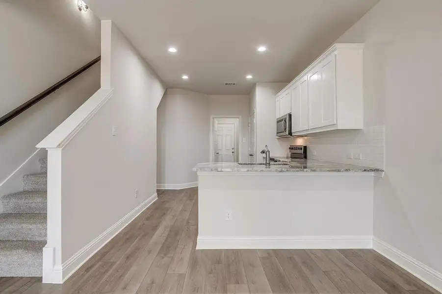 Kitchen with light stone counters, white cabinets, light wood finished floors, a peninsula, and recessed lighting