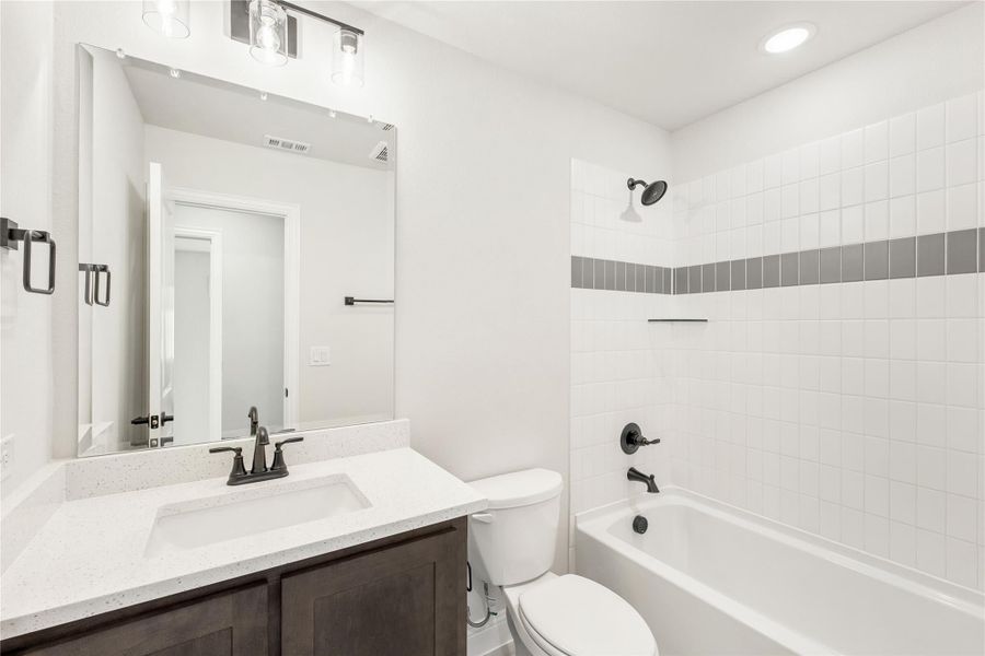 Bathroom with dark wood vanity, quartz countertop, and white tiled tub-shower combo with gray accent tile Bathroom with dark wood vanity, quartz countertop, and white tiled tub-shower combo with gray accent tile