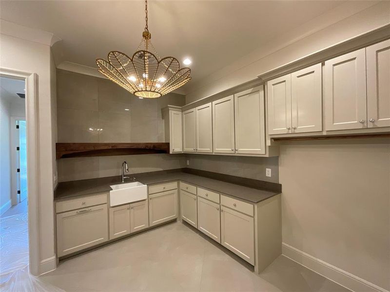 Kitchen with sink, a notable chandelier, white cabinetry, hanging light fixtures, and crown molding