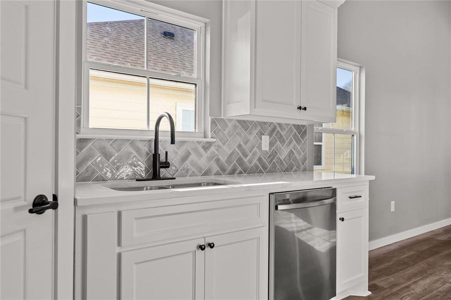 Kitchen featuring light stone counters, white cabinets, stainless steel dishwasher, and decorative backsplash