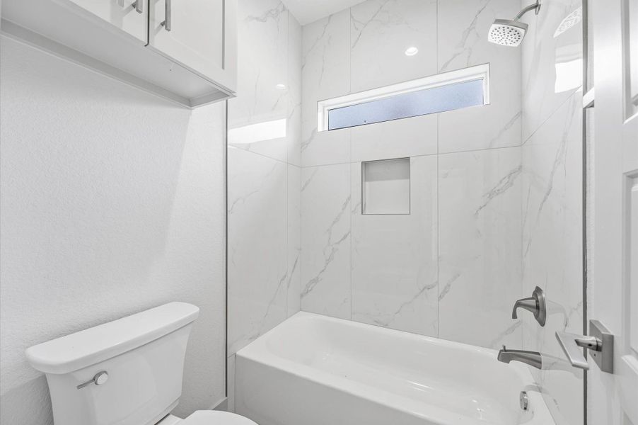 Modern bathroom with a sleek, marble-tiled shower and bathtub combo. It features a rain showerhead, built-in shelf, and a frosted window for natural light. The space includes a white toilet and cabinetry with silver hardware. Modern bathroom with a sleek, marble-tiled shower and bathtub combo. It features a rain showerhead, built-in shelf, and a frosted window for natural light. The space includes a white toilet and cabinetry with silver hardware.