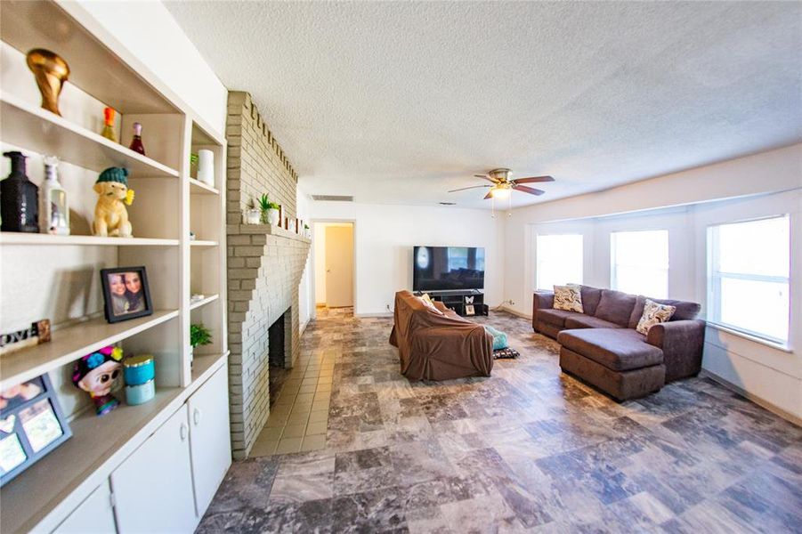 Living room featuring a textured ceiling, a fireplace, ceiling fan, and tile patterned flooring