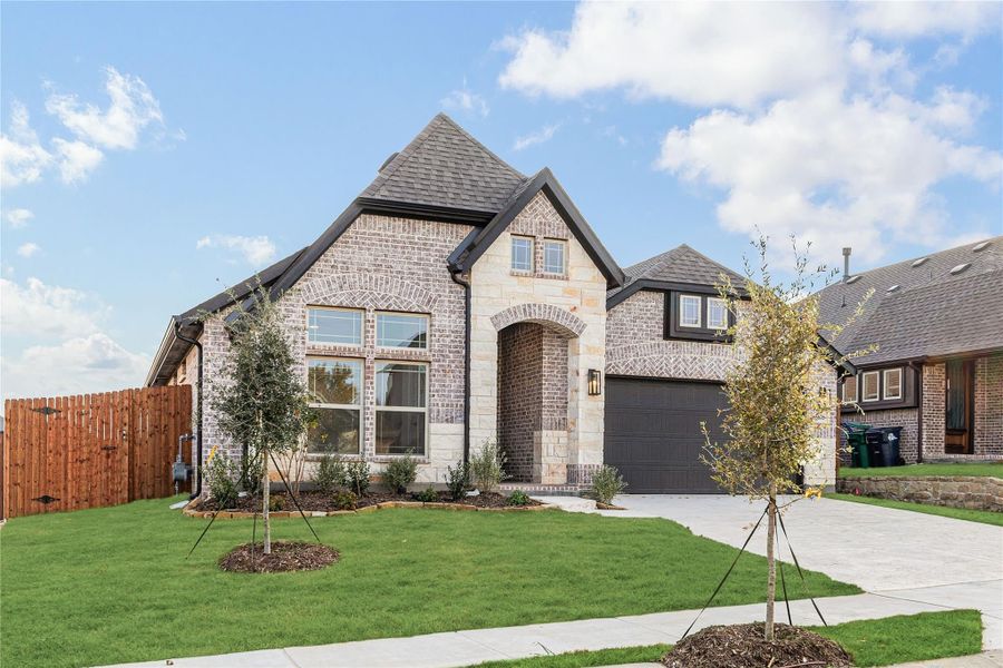 Two-story brick and stone home with arched entry, two-car garage, and manicured front lawn with young trees