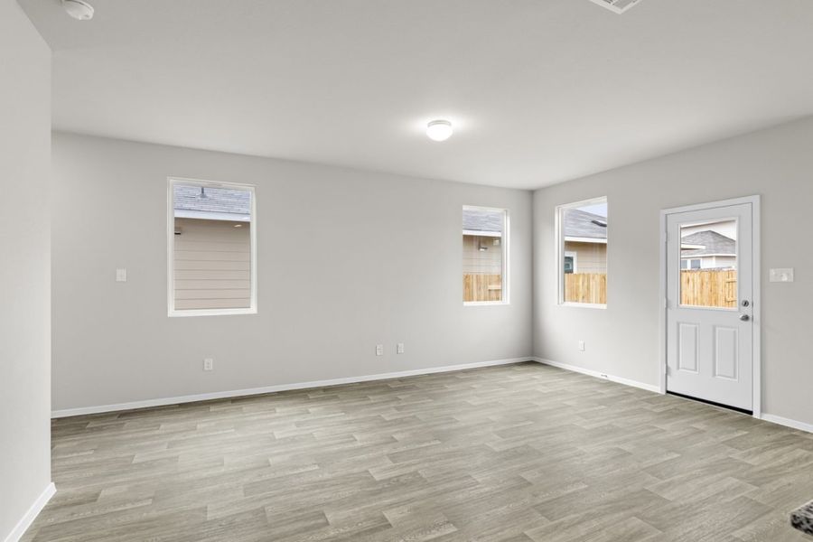 Image of a living room with cream walls, light brown flooring, windows, and a white back door