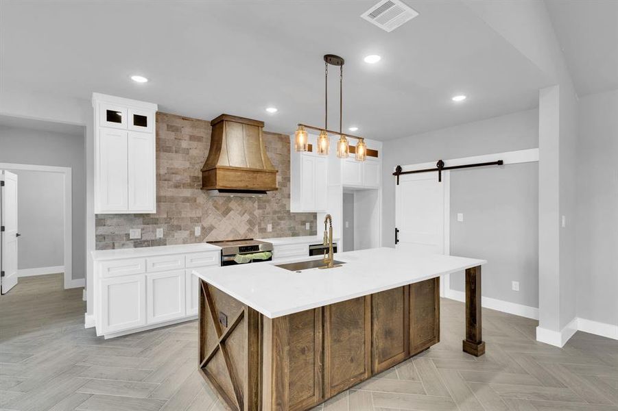 Kitchen with backsplash, a barn door, a center island with sink, white cabinetry, and recessed lighting