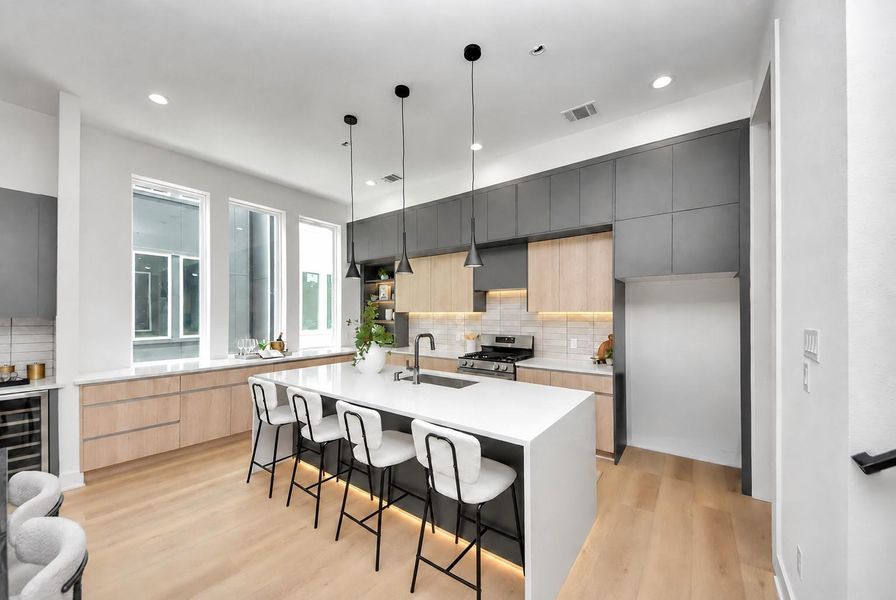 Modern kitchen featuring a spacious waterfall island, pendant lighting, two-tone cabinetry, and stainless steel appliances.