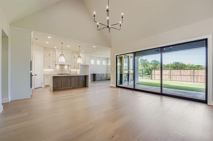Unfurnished living room with high vaulted ceiling, a chandelier, light wood-type flooring, and recessed lighting