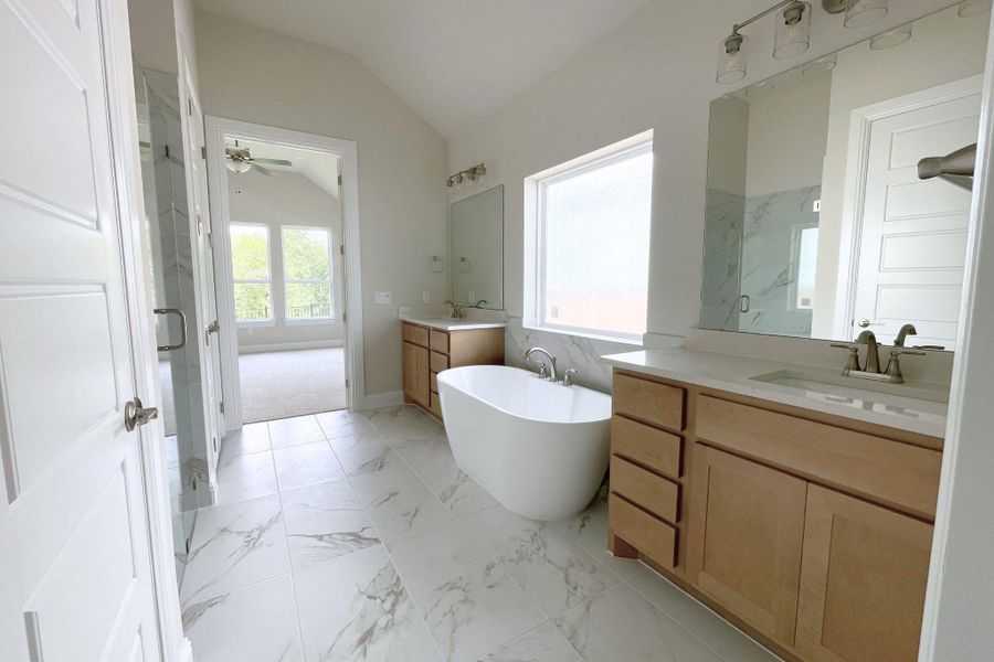 A spacious primary bathroom boasts dual vanities, a luxurious soaking tub, and elegant tile flooring.