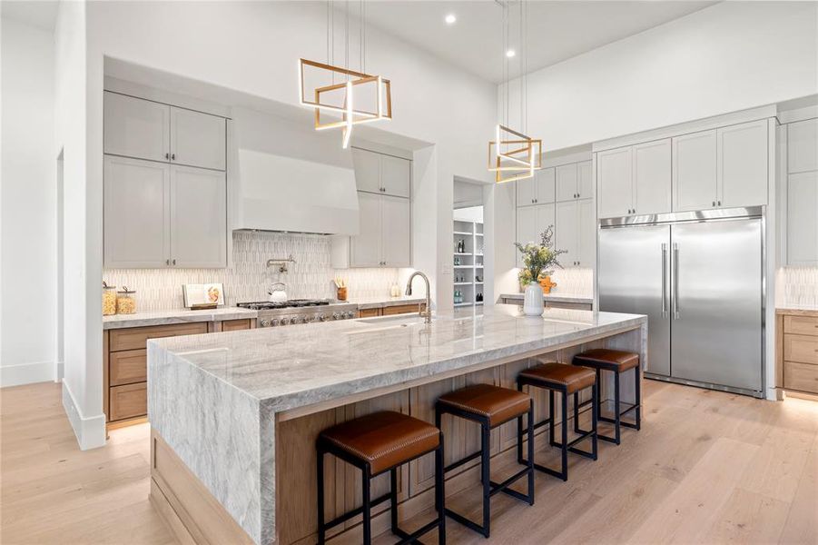 Kitchen with a kitchen bar, light stone counters, stainless steel appliances, a large island, and backsplash