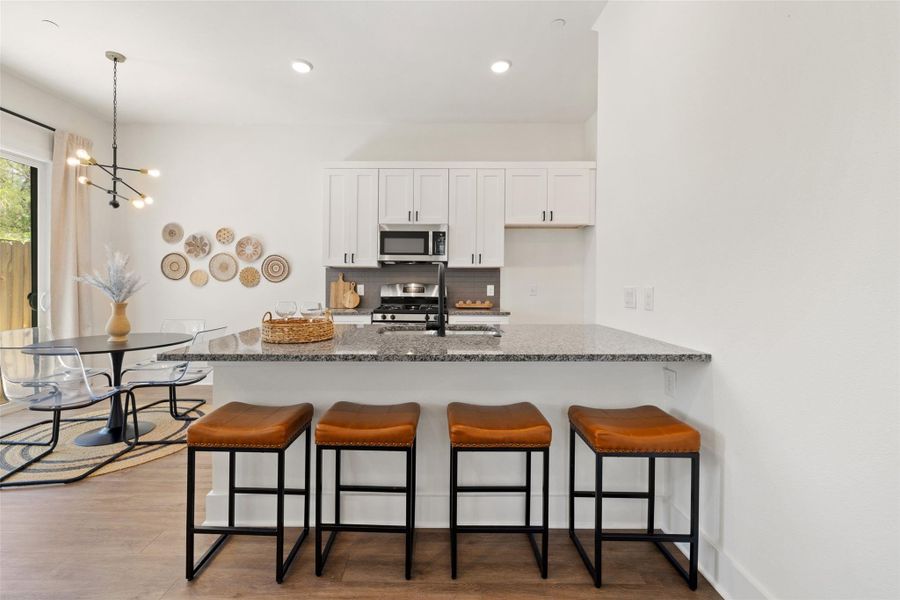 Kitchen with wood finished floors, a kitchen breakfast bar, white cabinets, dark stone countertops, and recessed lighting Kitchen with wood finished floors, a kitchen breakfast bar, white cabinets, dark stone countertops, and recessed lighting