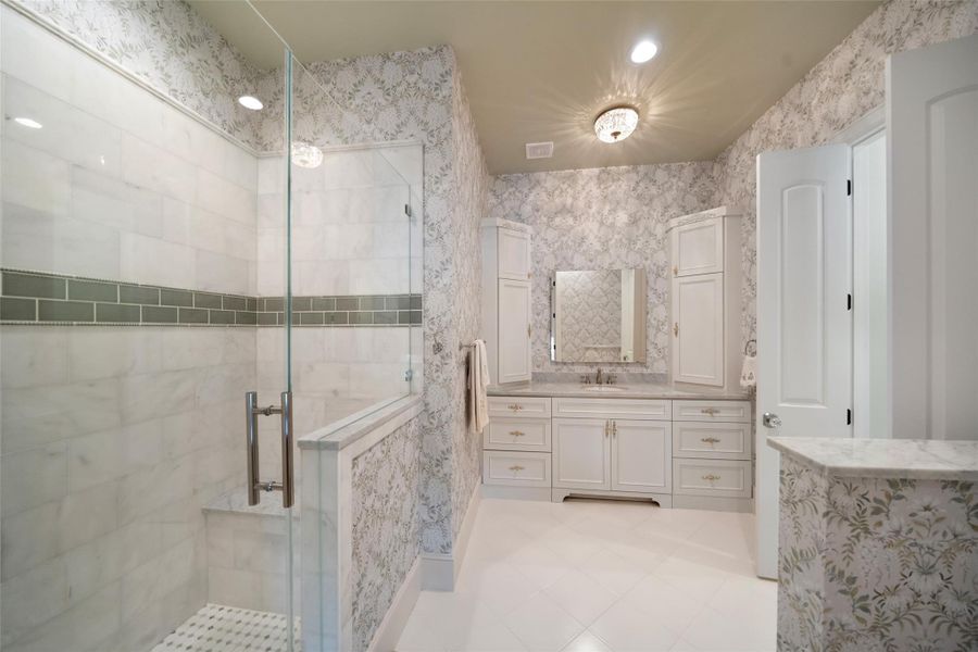 This en-suite bathroom is filled with natural light, featuring a walk-in shower, beautiful vanity, and tasteful wallpaper.