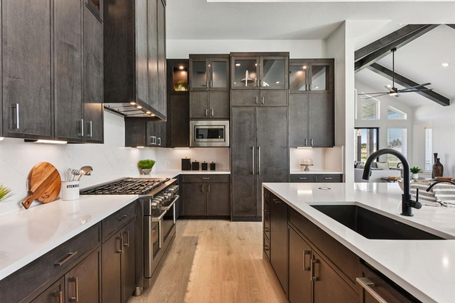 Kitchen featuring dark wood finish cabinets, built in appliances, light wood-style floors, and vaulted ceiling with beams