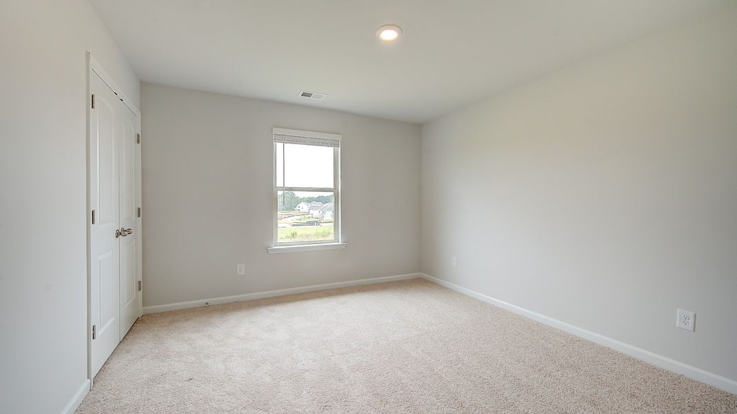 Secondary bedroom with carpet flooring and window providing natural light in the Meridian II at Brighton in Locust Grove, GA.
