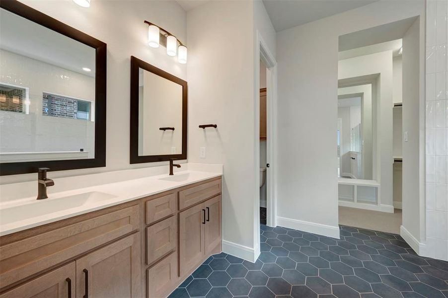 Full bathroom with double vanity, dark tile patterned floors, and a walk in closet