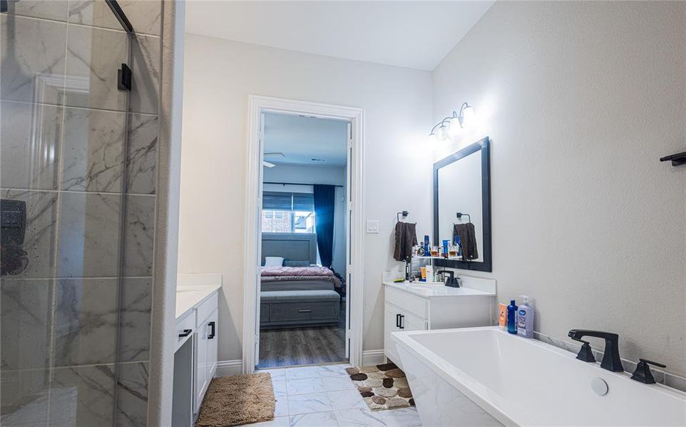 Ensuite bathroom featuring vanity, light marble finish floors, a soaking tub, and a marble finish shower