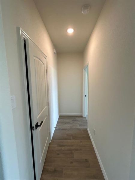 Hallway featuring wood-finish flooring, recessed lighting, white walls, and a paneled door with matte black hardware