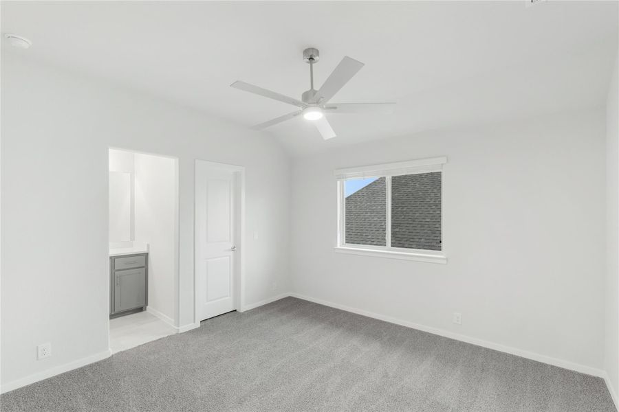 Empty bedroom with gray carpet, ceiling fan, and attached bathroom visible through doorway