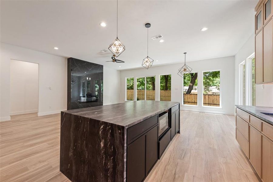 Kitchen with recessed lighting, light wood-style floors, a center island, hanging light fixtures, and glass insert cabinets